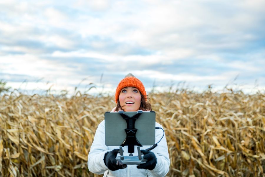 A female pilot using a drone remote controller with a tablet screen and gazing upwards in awe.