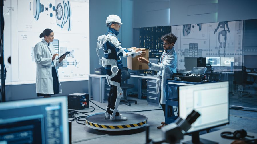 Des ingénieurs travaillent sur un exosquelette robotisé en laboratoire. Une personne le met à l’essai en tentant de soulever une boîte de carton.