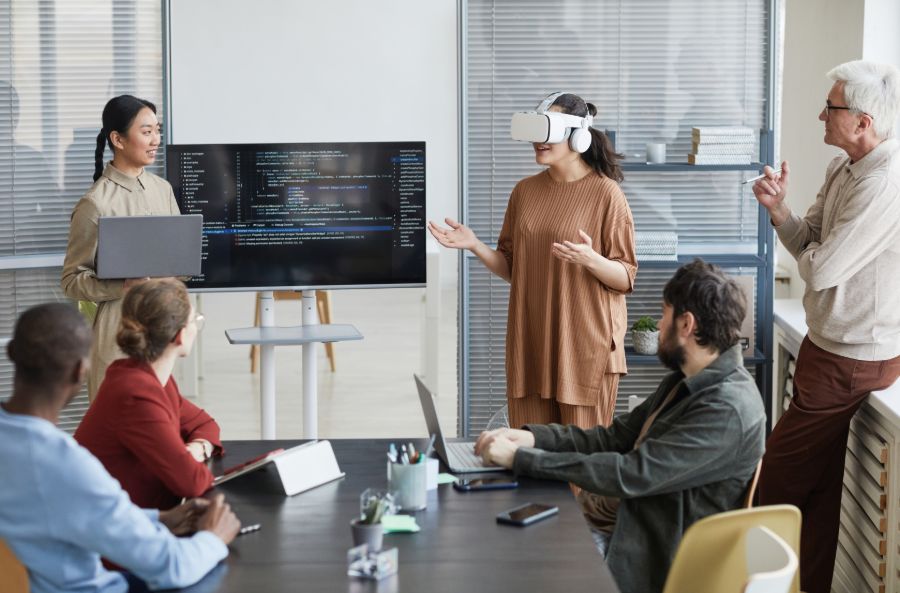 Dirigeante d’une entreprise en démarrage utilisant un casque de réalité virtuelle pendant une réunion de projet avec une équipe de développement de logiciels.