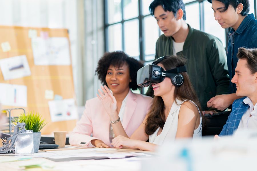 Groupe multiethnique de jeunes femmes et hommes professionnels dans un bureau utilisant un casque de réalité virtuelle.