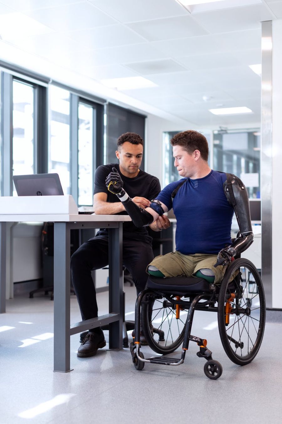Male professional adjusting prosthetic arm for a disabled person in a wheelchair.