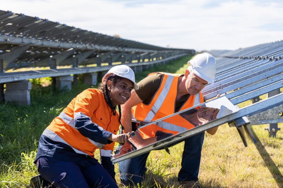 Un ingénieur senior et une jeune apprentie travaillant ensemble sur l’installation d’une ferme solaire.