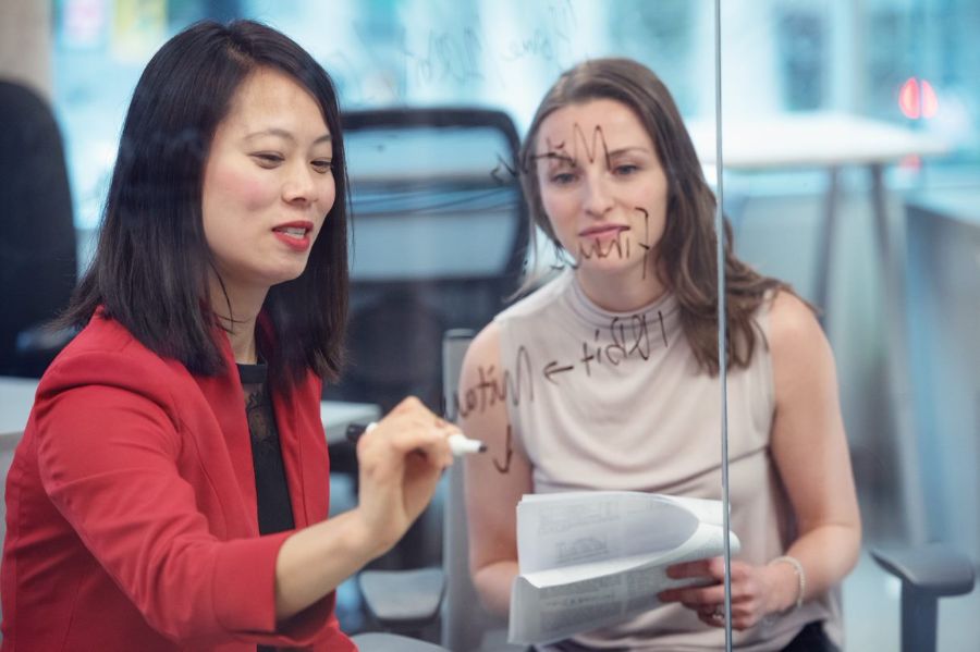 Une femme d’affaires asiatique et une femme d’affaires blanche écrivant sur un tableau.