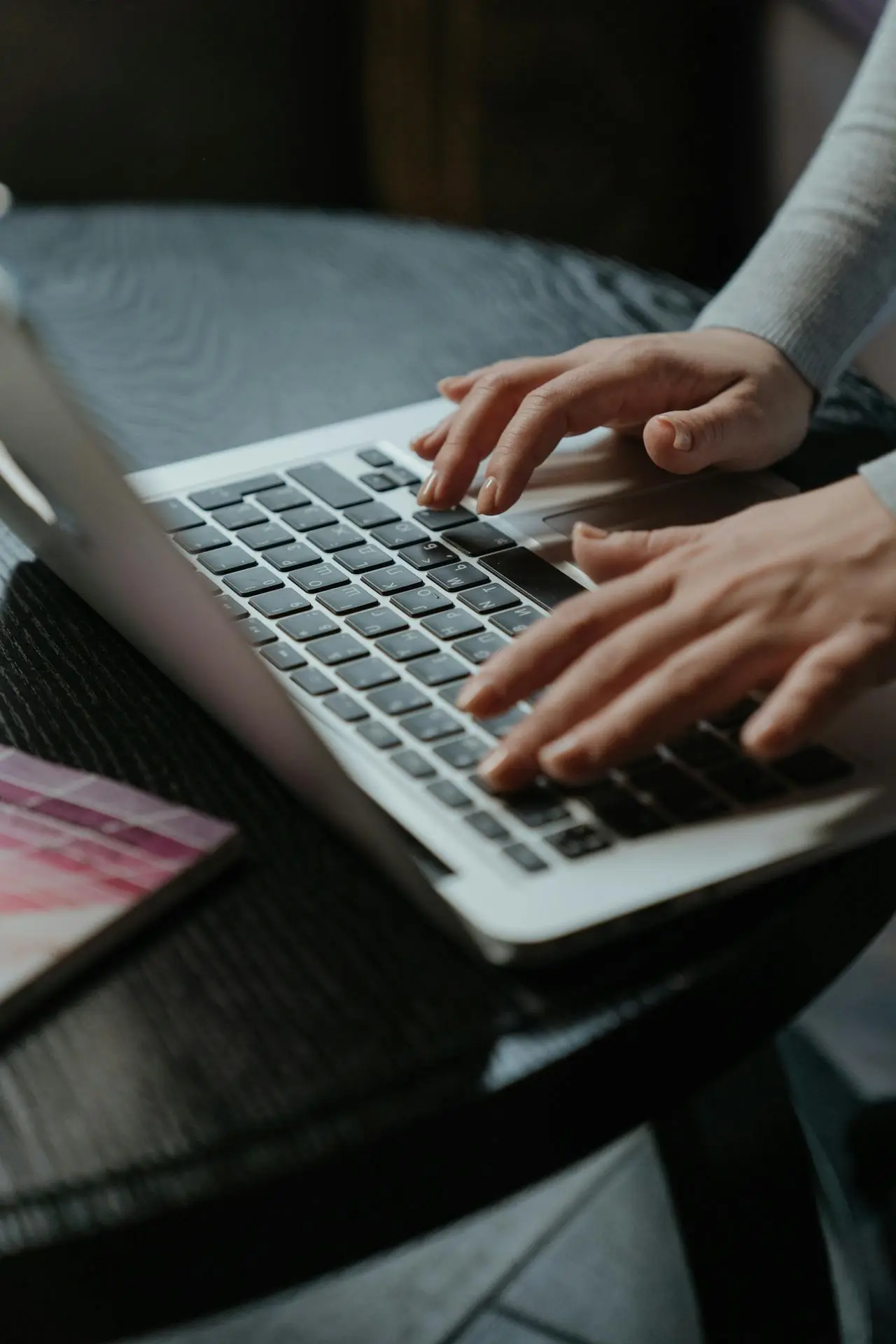A person typing on a laptop at a round black table, exploring faculty research opportunities, with a notebook and pen nearby. Only their hands and part of their arms are visible.