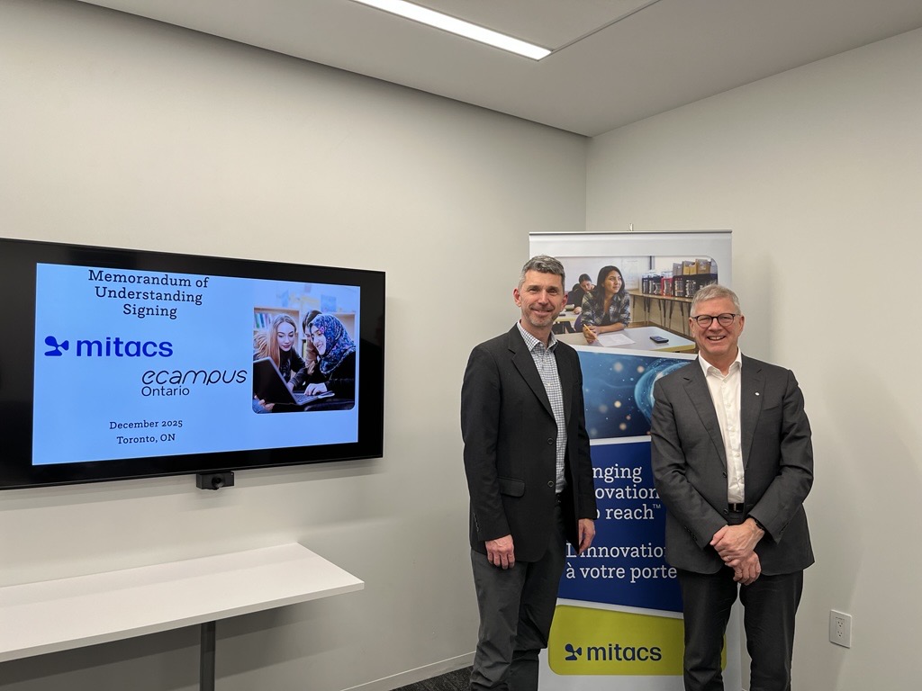 Two men in business attire stand and smile in an office beside a banner and a screen displaying Memorandum of Understanding Signing, Mitacs, eCampusOntario, highlighting the Mitacs Strategic Plan 2026-2030 Talent and Research Powering Innovation.