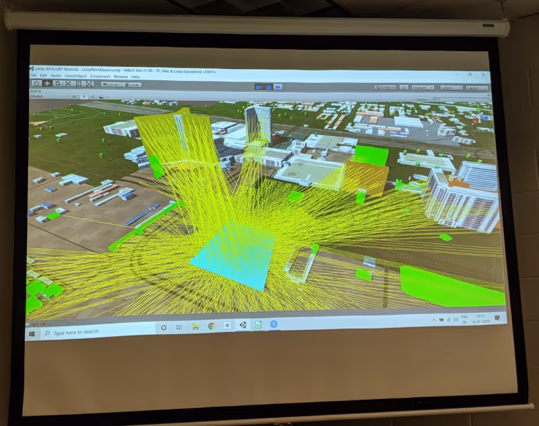 A projected computer simulation shows a 3D city model with green buildings and yellow lines radiating from a central point, likely visualizing data or signal paths. A Windows taskbar is visible at the bottom of the screen.